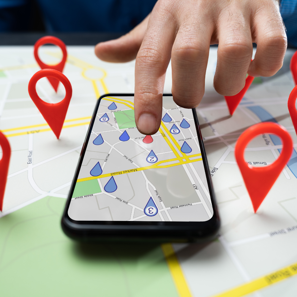 Person's hand on a smartphone map with red and blue location markers. Map is surrounded by red pin markers.