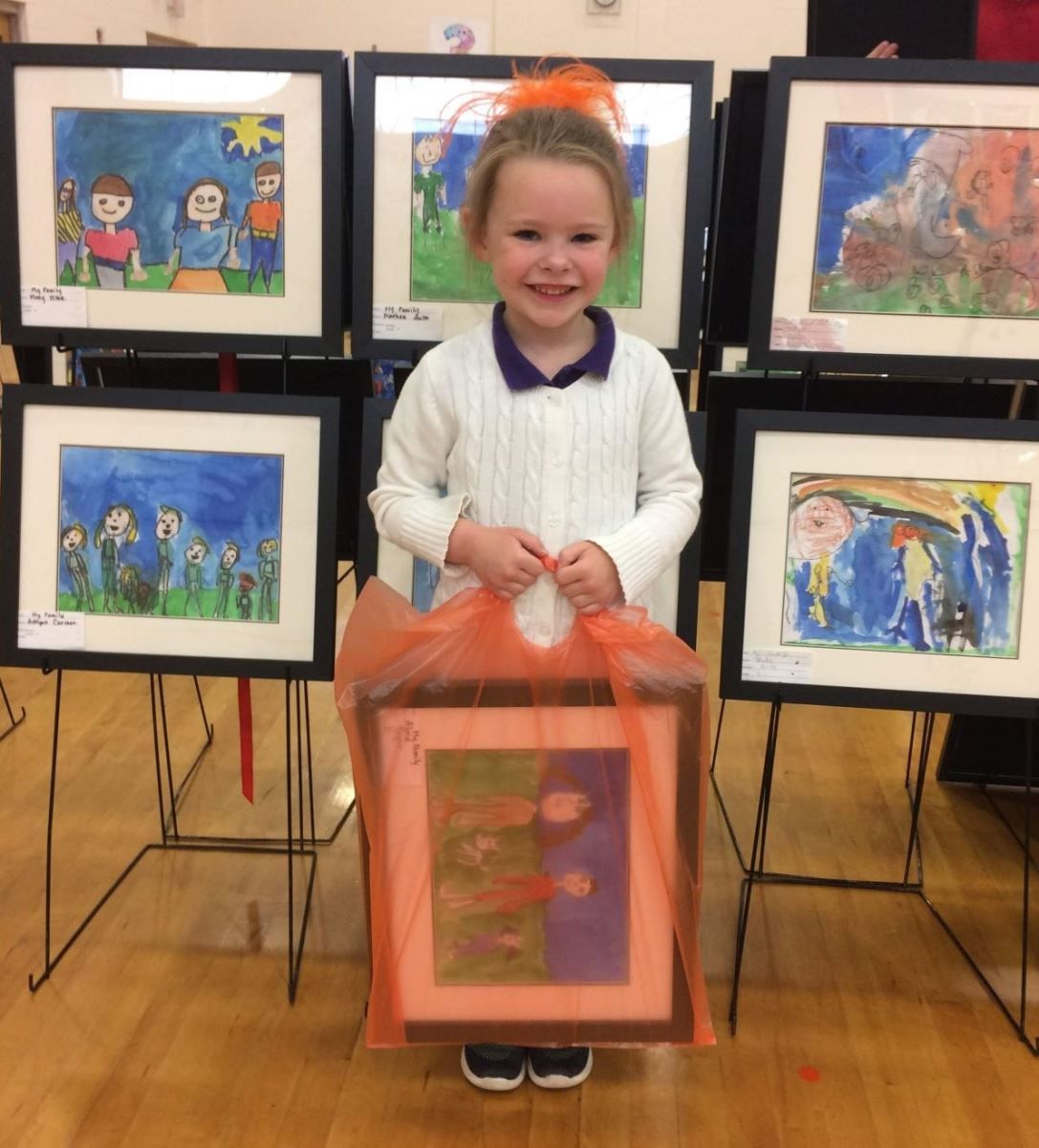 a little girl is holding a framed picture in front of a display of children 's artwork