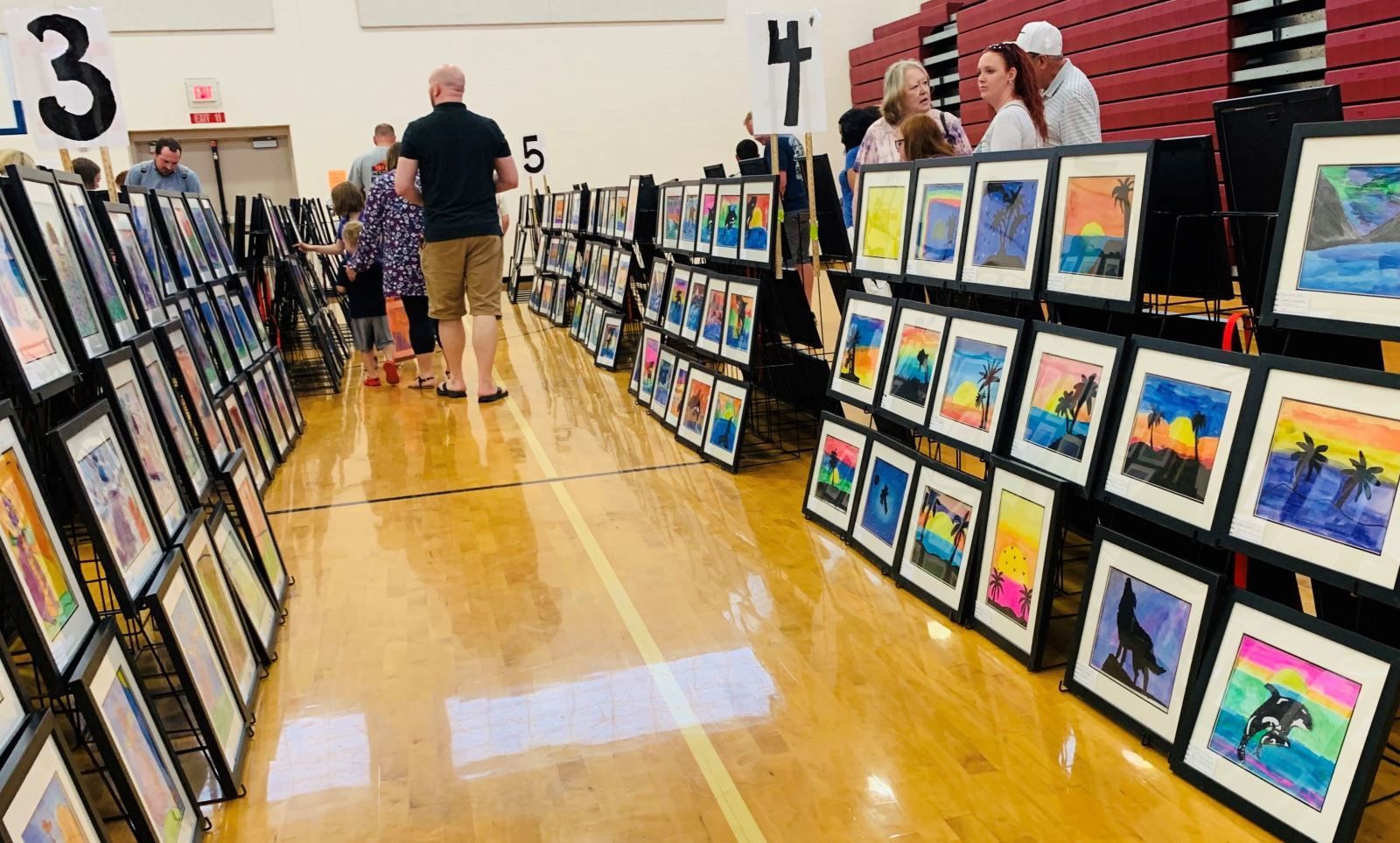 a group of people are looking at paintings on display in a gym .