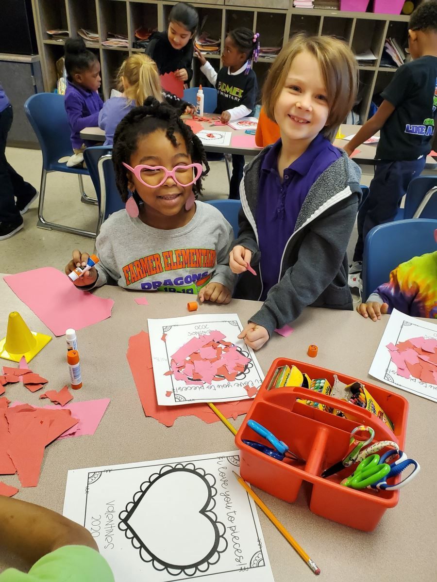a group of children are sitting at a table making valentine 's day crafts