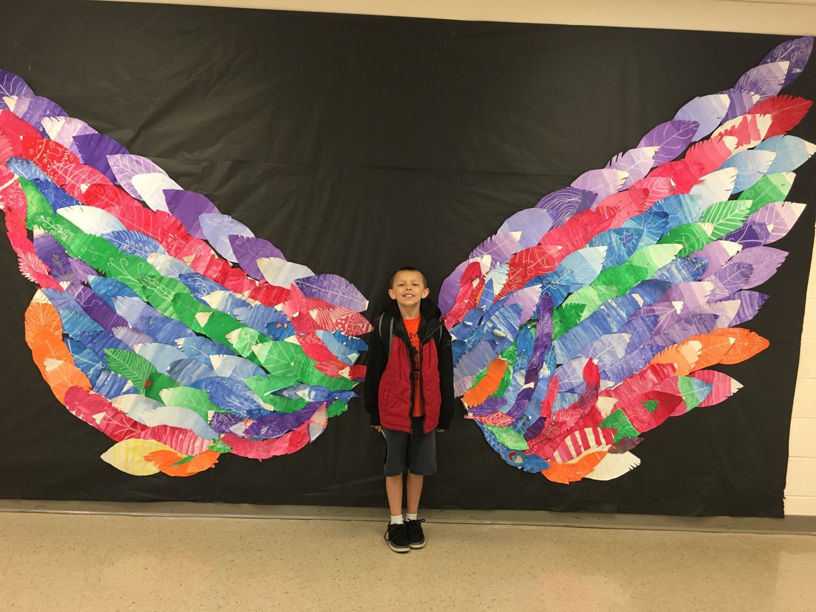 a young boy is standing in front of a large painting of wings .