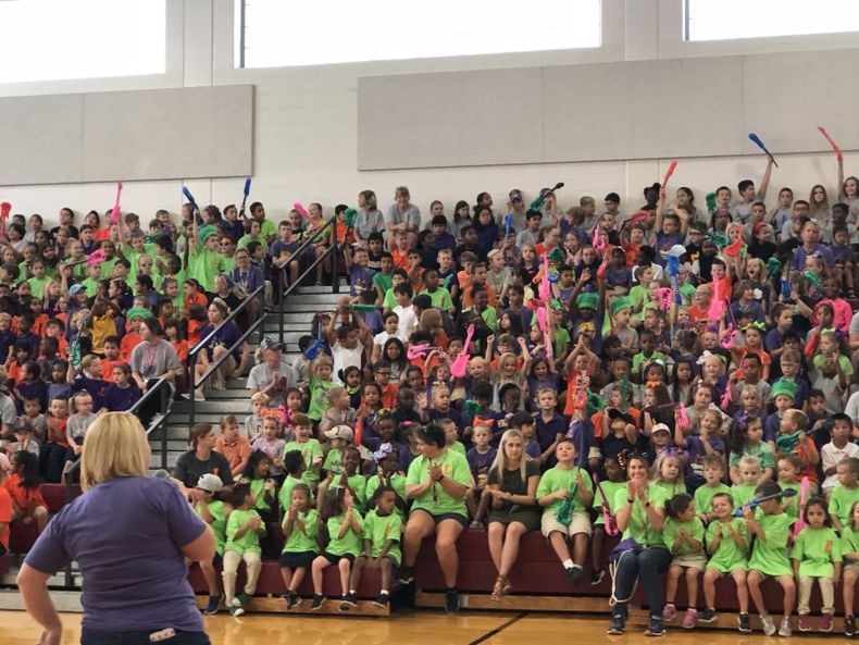 a woman stands in front of a large crowd of children in green shirts