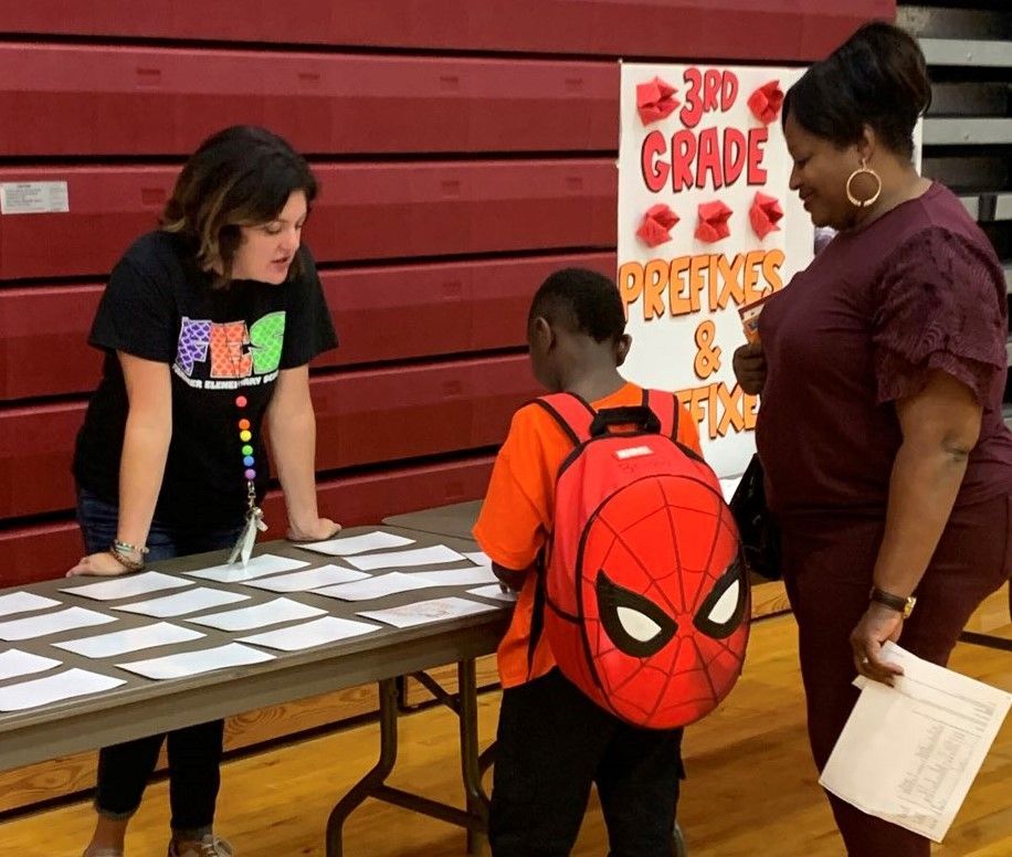 a boy with a spider man backpack is standing at a table with two women