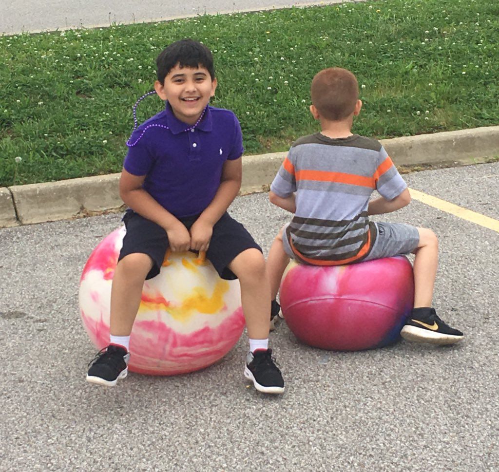 two young boys are sitting on bouncy balls in a parking lot