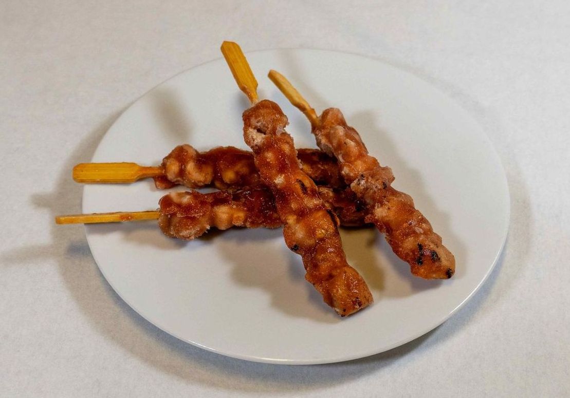 Trois brochettes de poulet sur une assiette blanche sur une table