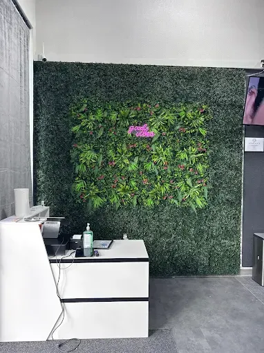 Reception desk with white counter, faux greenery wall, neon sign, and hand sanitizer.