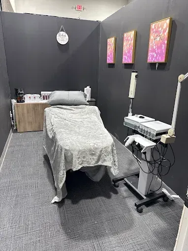 Aesthetician's treatment room: gray walls, bed with blanket, equipment, artwork.