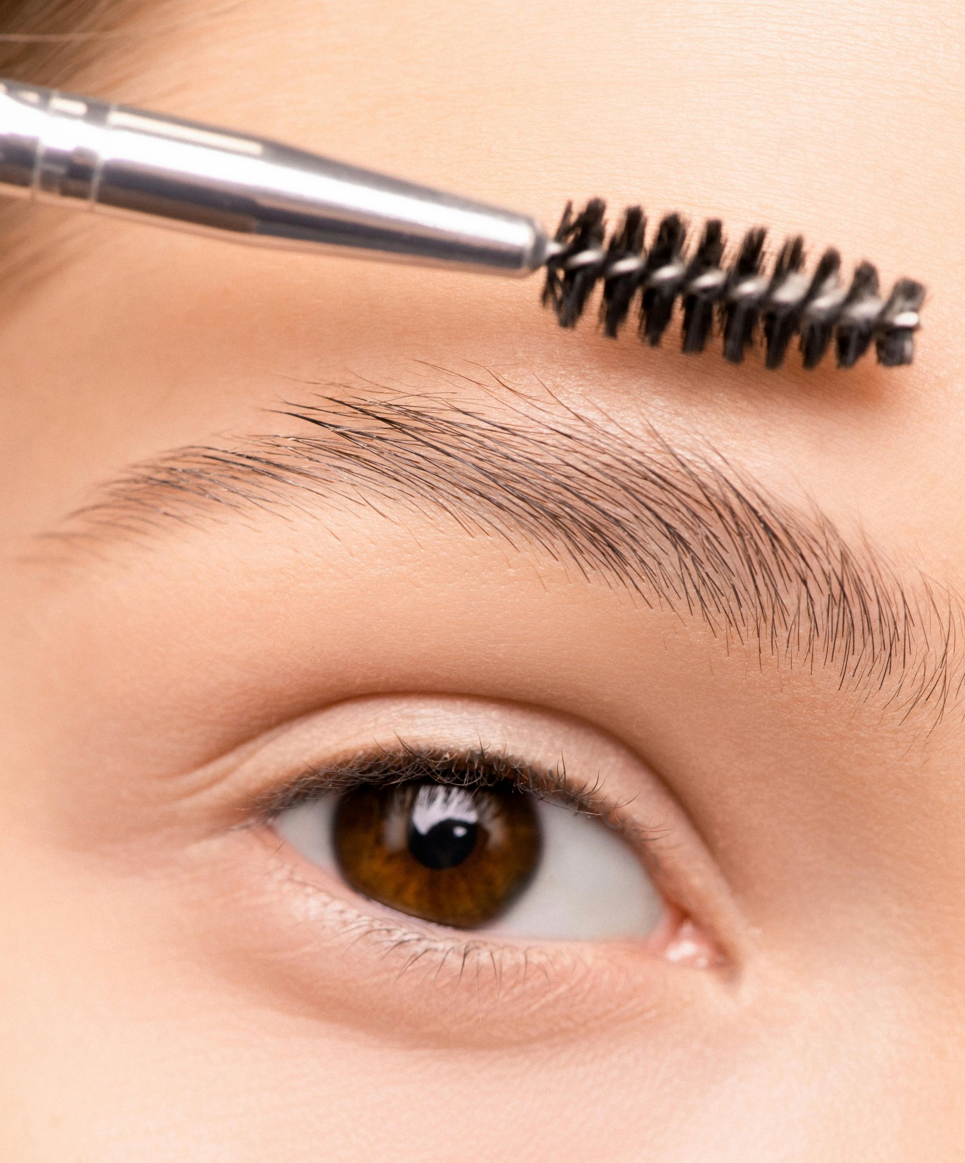 Close-up of a person's eye and eyebrow being groomed with a spoolie brush. Brown eye, fair skin.