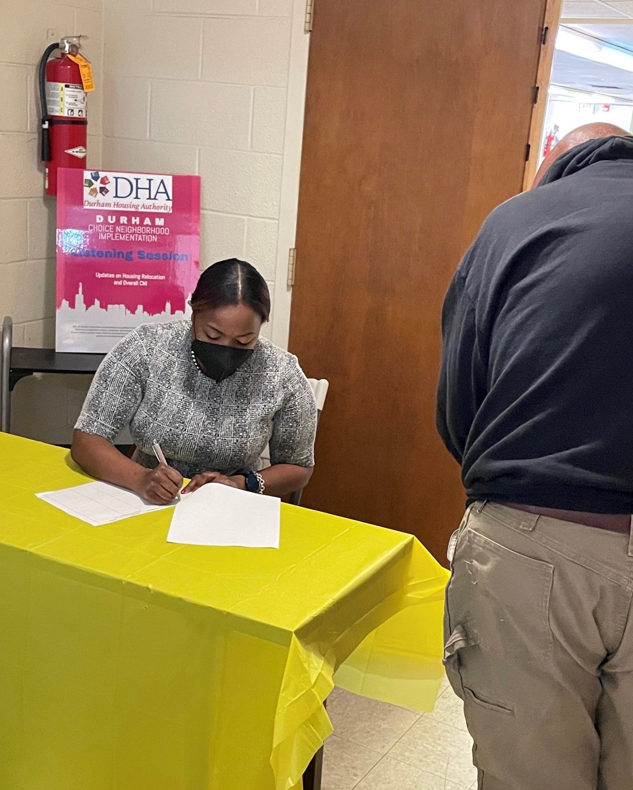 A woman wearing a mask is sitting at a table signing papers.