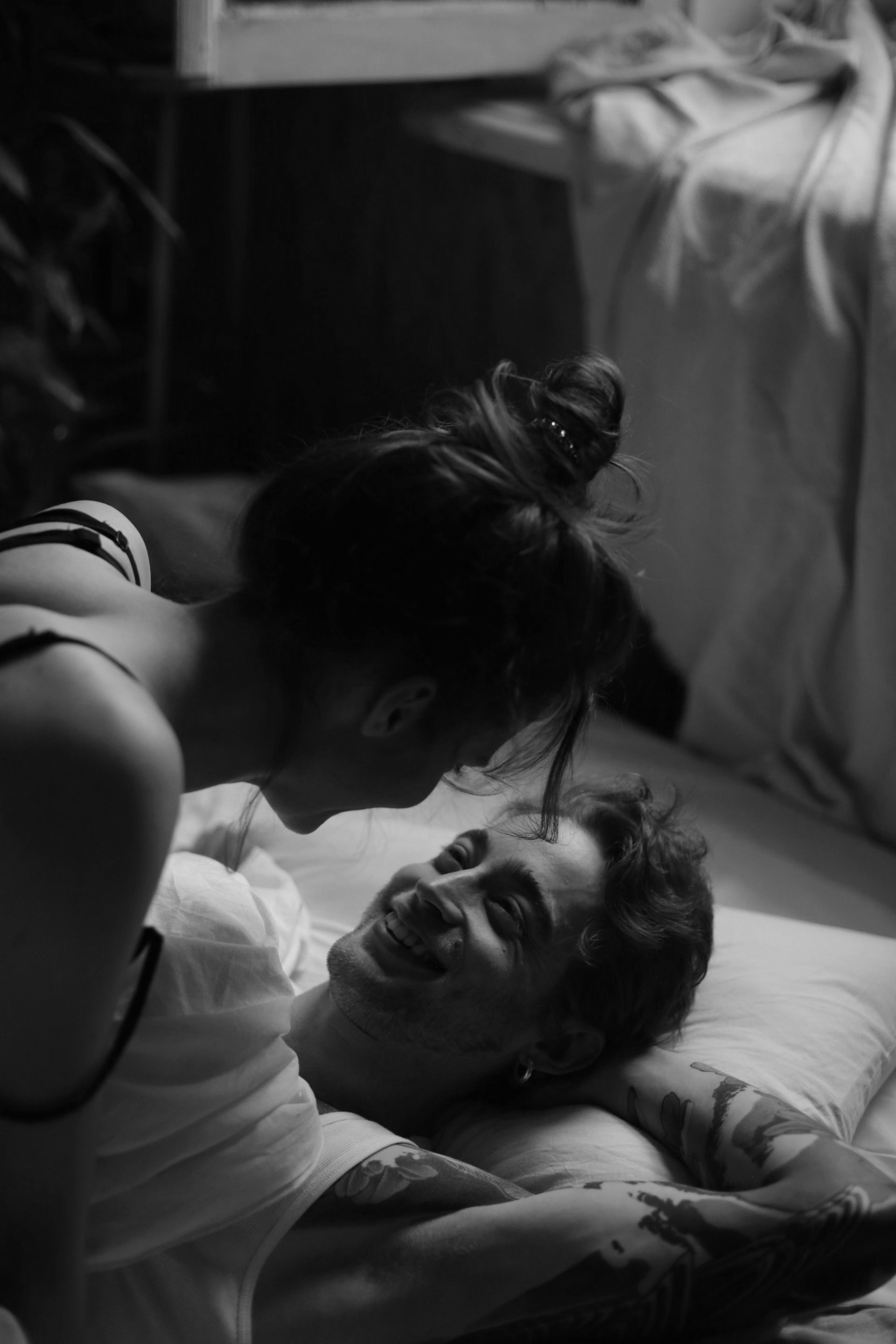 A couple smiling at each other in a bed, woman leaning over man. Black and white photo.