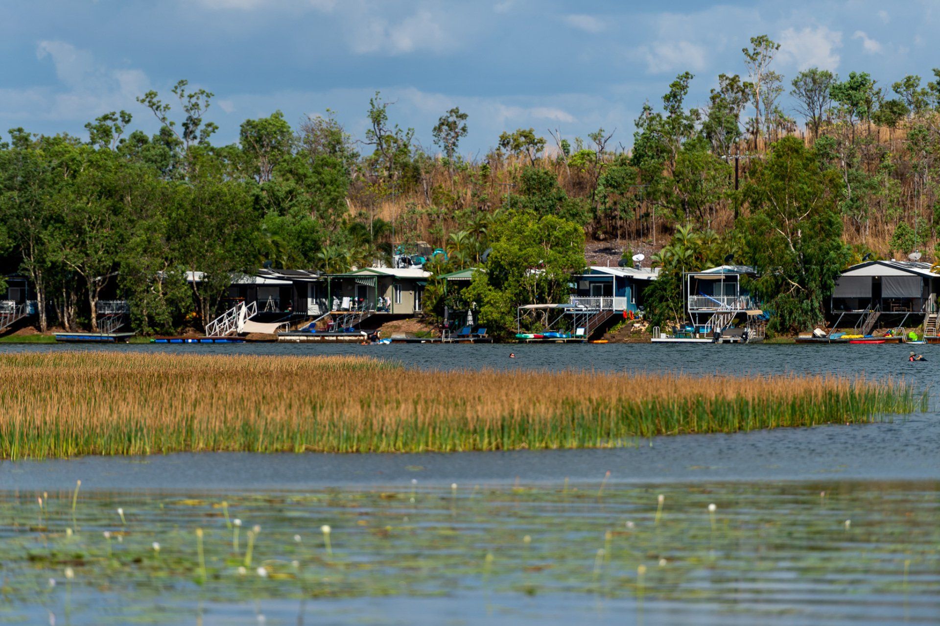A row of houses sit on the shore of a lake surrounded by trees.