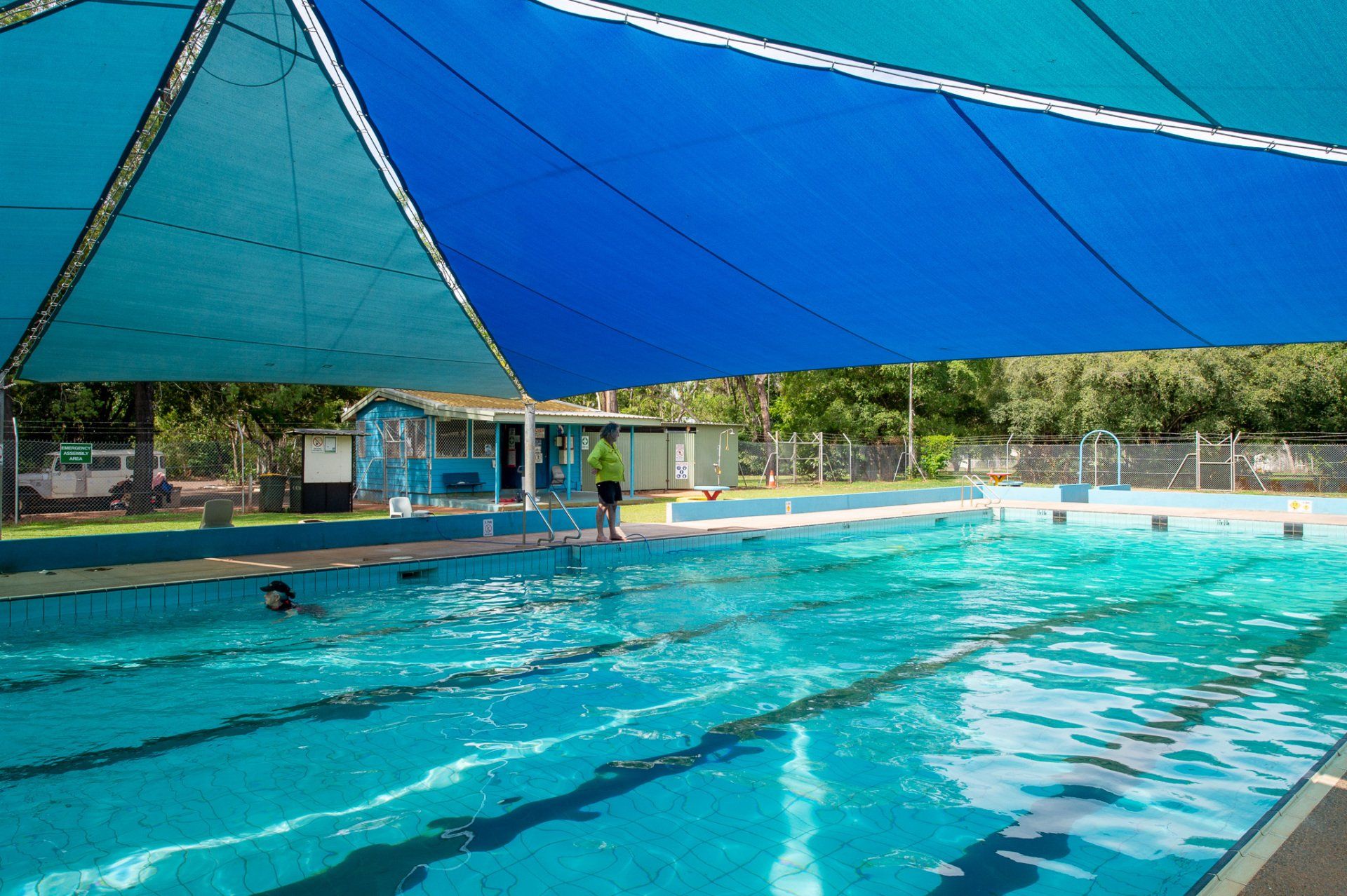 A person is swimming in a swimming pool under a blue umbrella.