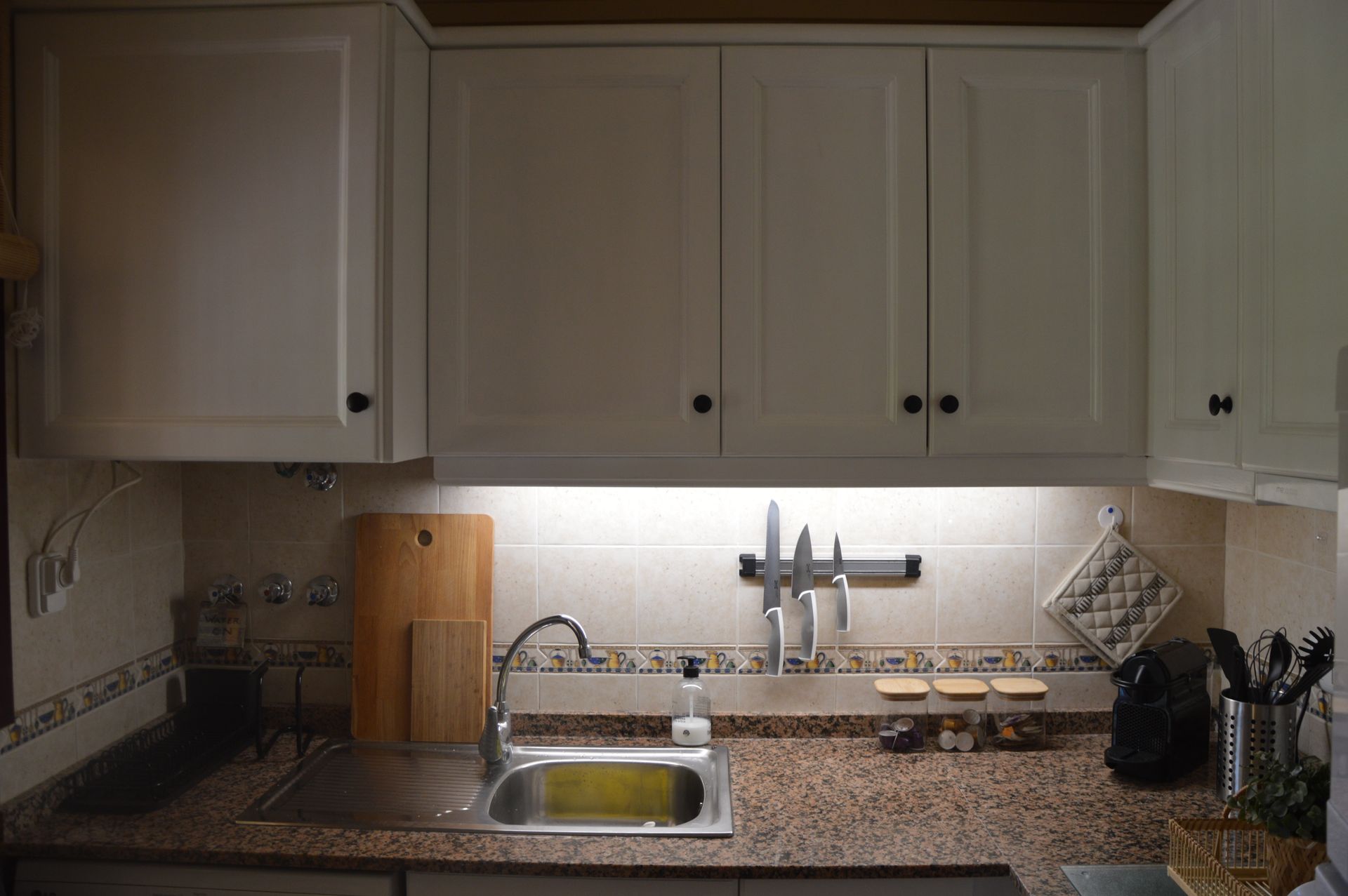 Een keuken met granieten aanrechtbladen, witte kasten, een gootsteen en een snijplank.