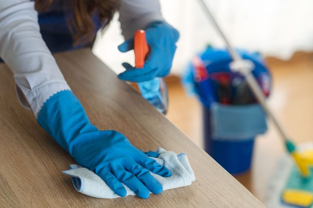 A woman in blue gloves is cleaning a wooden table with a cloth.