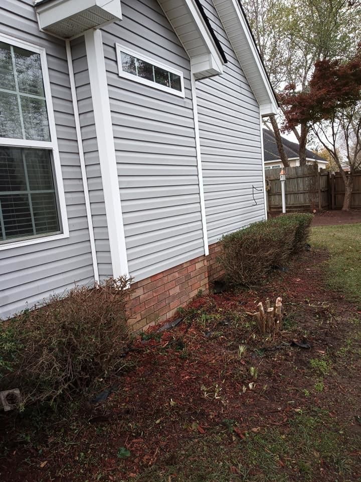 The side of a house with a lot of bushes in front of it.