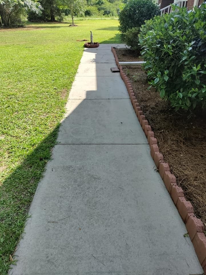 A sidewalk leading to a grassy field with a brick border.