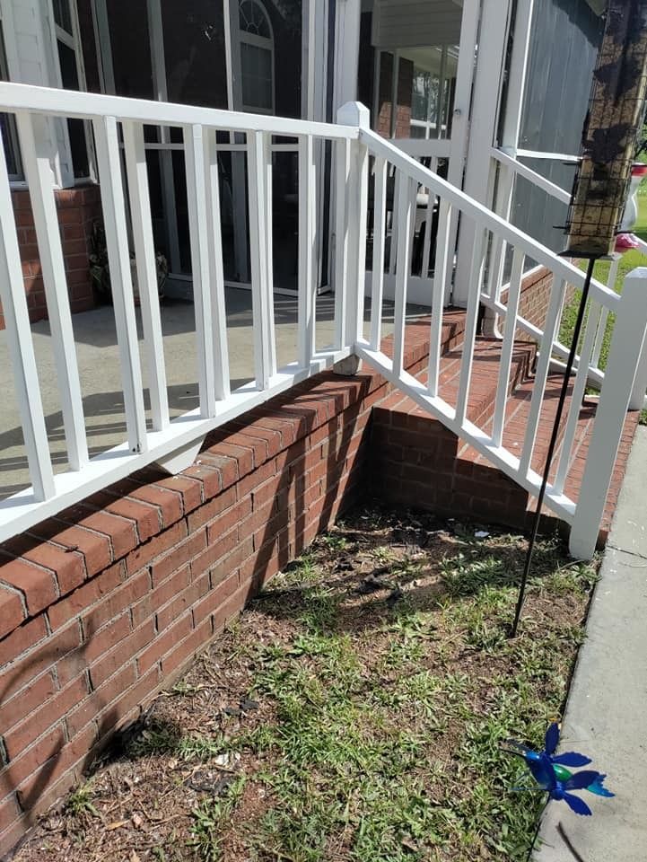 A white railing on a porch next to a brick wall.