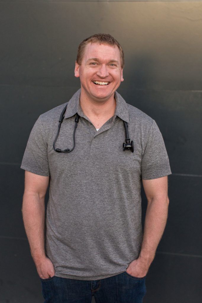 A man wearing a gray shirt and a stethoscope around his neck is smiling.