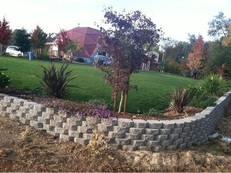 A Stone Wall Surrounds a Lush Green Field with A House in The Background - Oroville, CA - JR Landscaping 