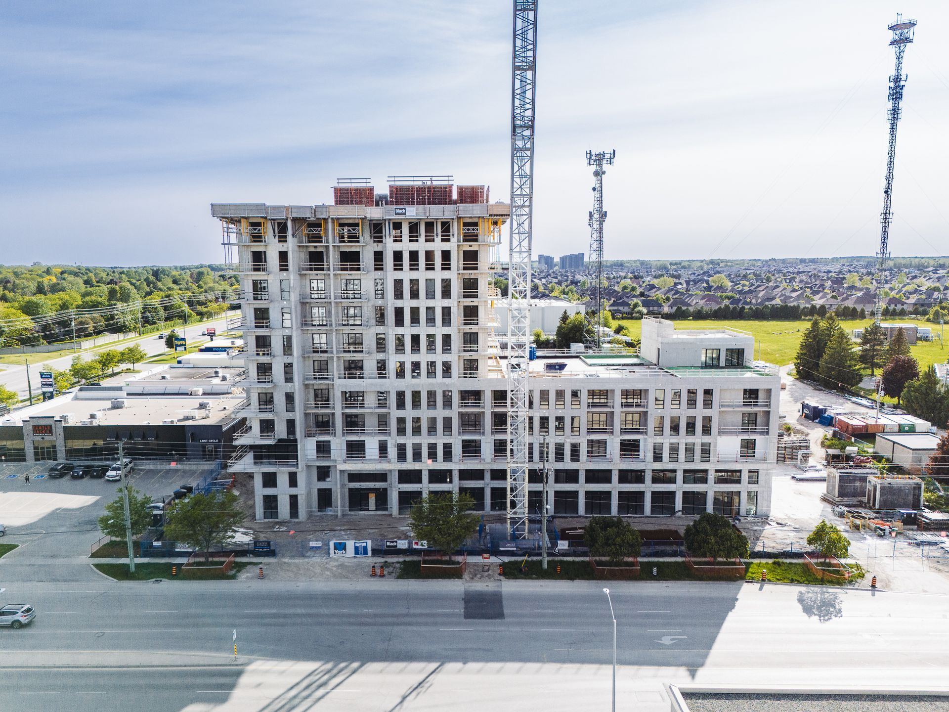 Abandoned high-rise building under construction with cranes on a wide roadway beside trees