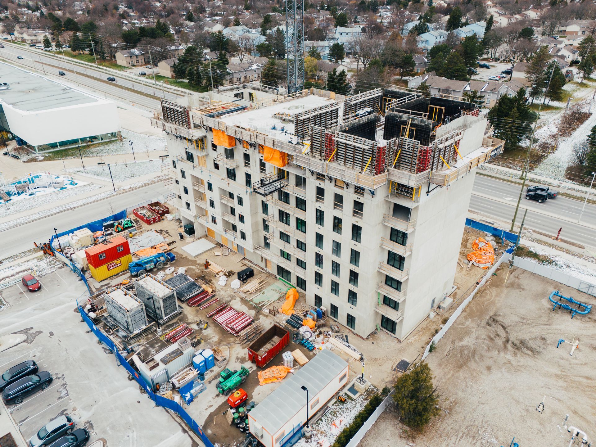 Aerial view of a multi-story building under construction with cranes, equipment, and snow-covered ground