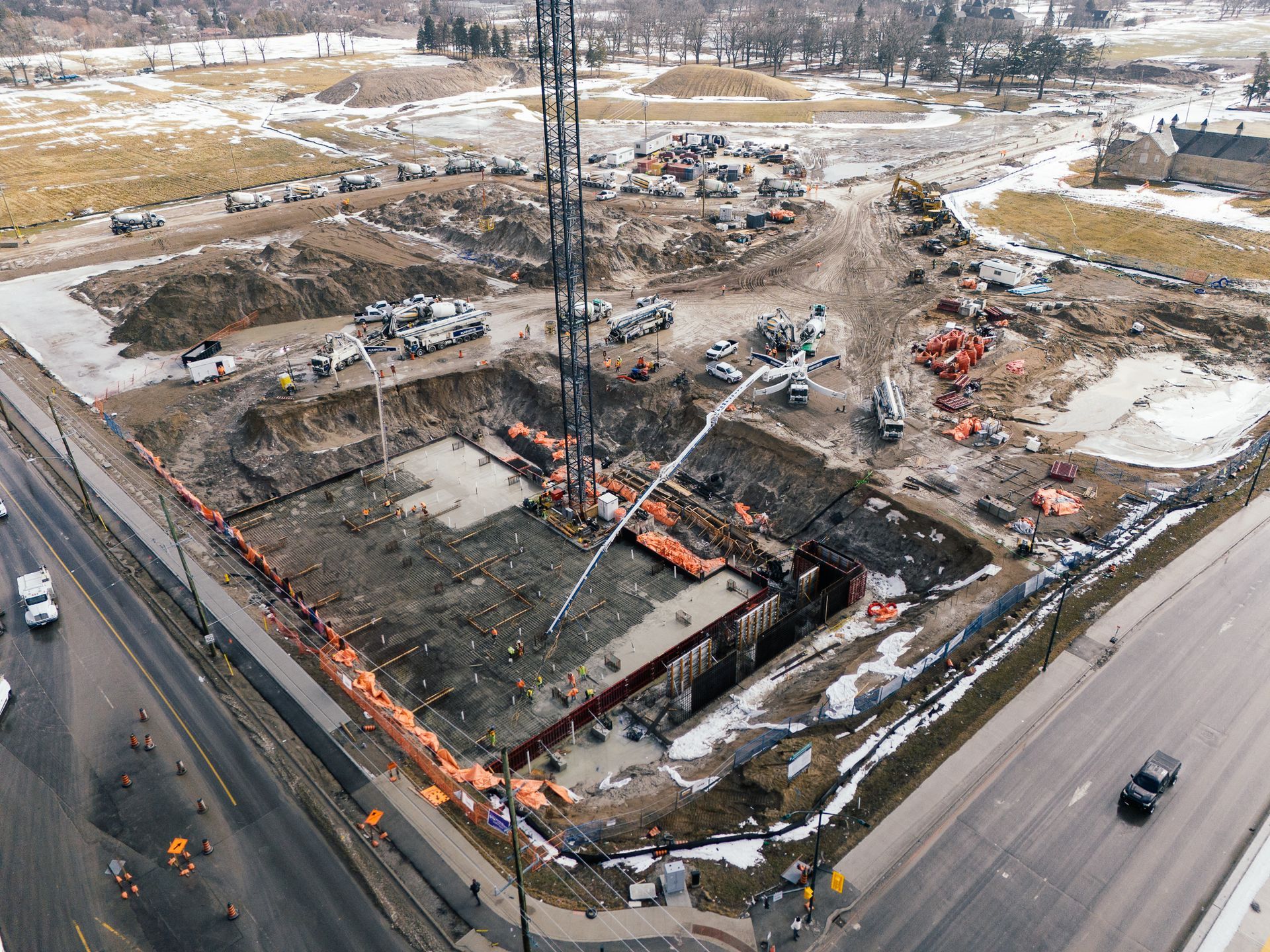 Aerial view of a construction site with excavators, a tall crane, and roads around the work area.
