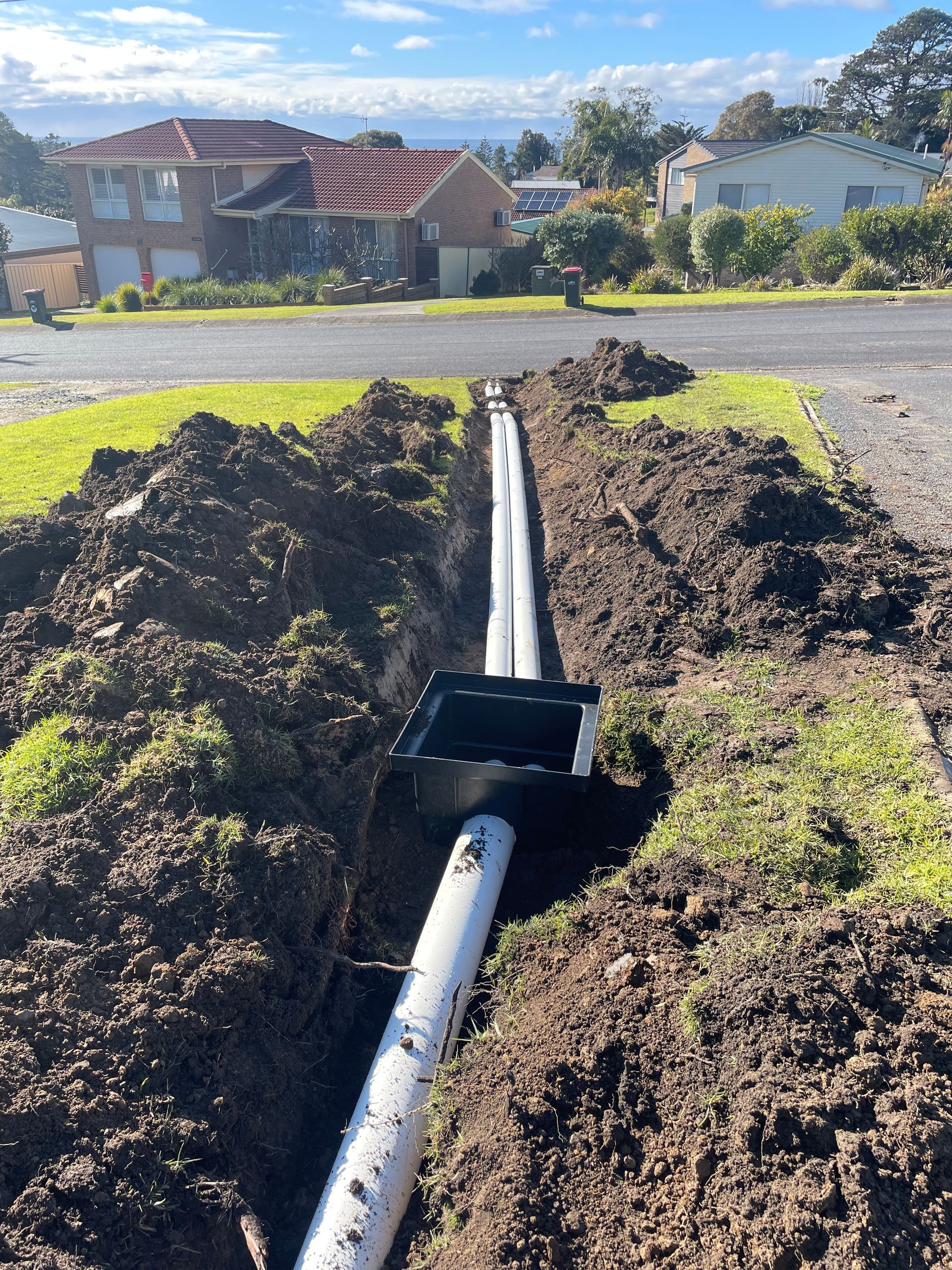 A white pipe is laying in the dirt next to a house.
