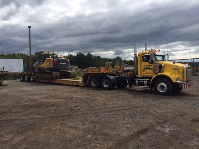 Un camion jaune transporte une excavatrice jaune sur une remorque.