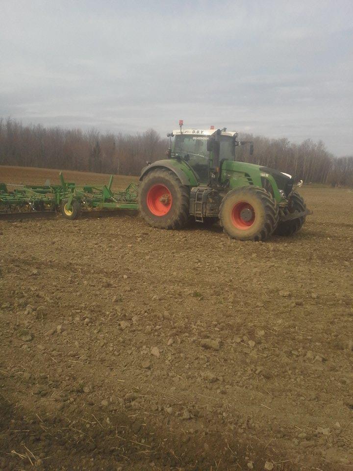 Un tracteur vert laboure un champ avec une remorque attachée.