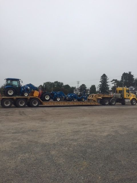Un camion jaune transporte des tracteurs bleus sur une remorque à plateau.