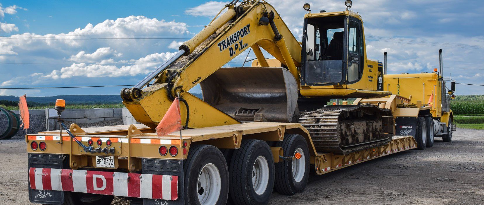 Une excavatrice jaune est assise sur un camion à plateau.