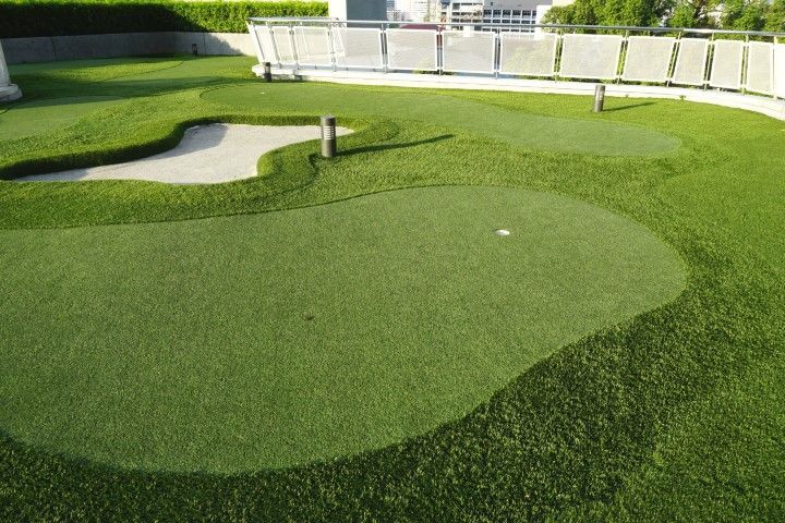 A miniature golf putting green with artificial turf, a small sand trap, and two holes, located on an outdoor rooftop deck.