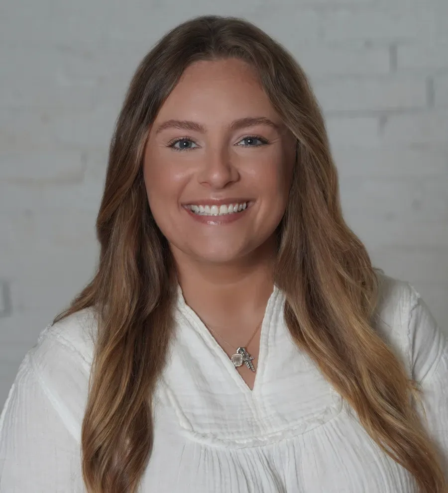 A woman wearing a black turtleneck and a white jacket is smiling for the camera.