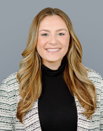 A woman wearing a black turtleneck and a white jacket is smiling for the camera.