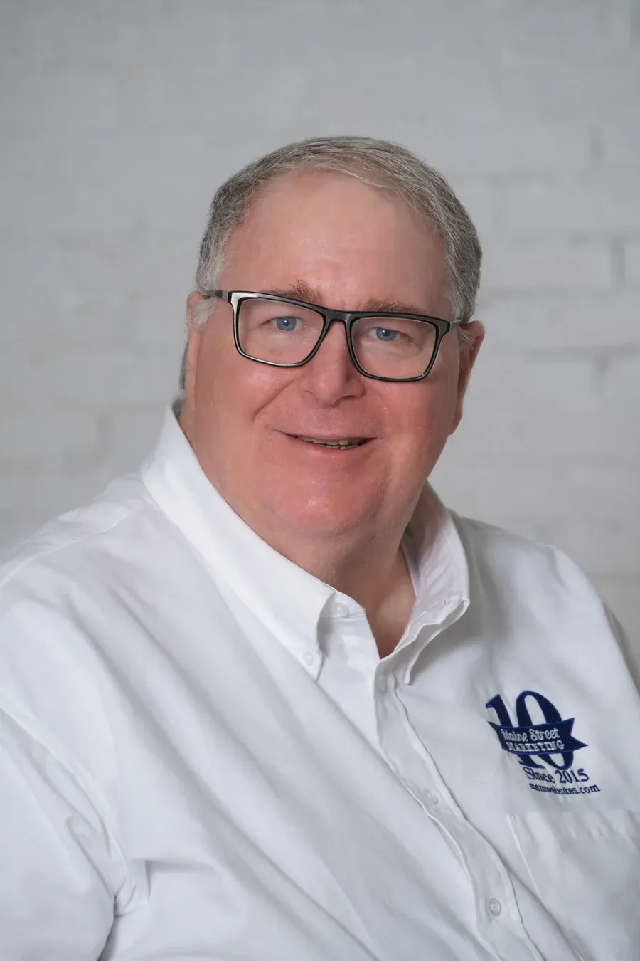 A man wearing glasses and a white shirt is smiling for the camera.