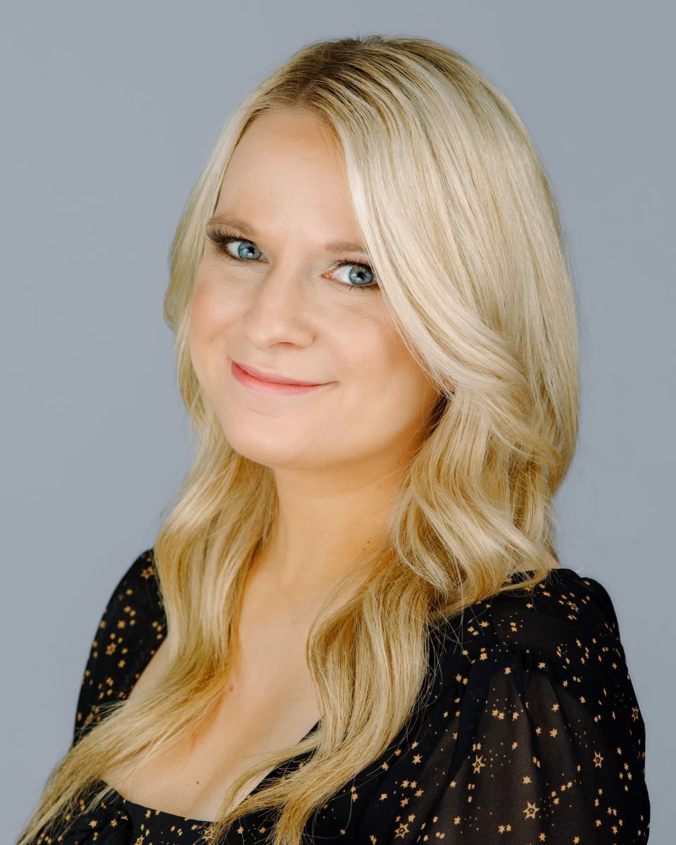 A woman with blonde hair and blue eyes is wearing a black top.