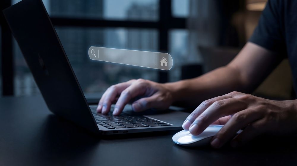 Hands typing on a laptop beside a white mouse in a dimly lit workspace with a search bar overlay.