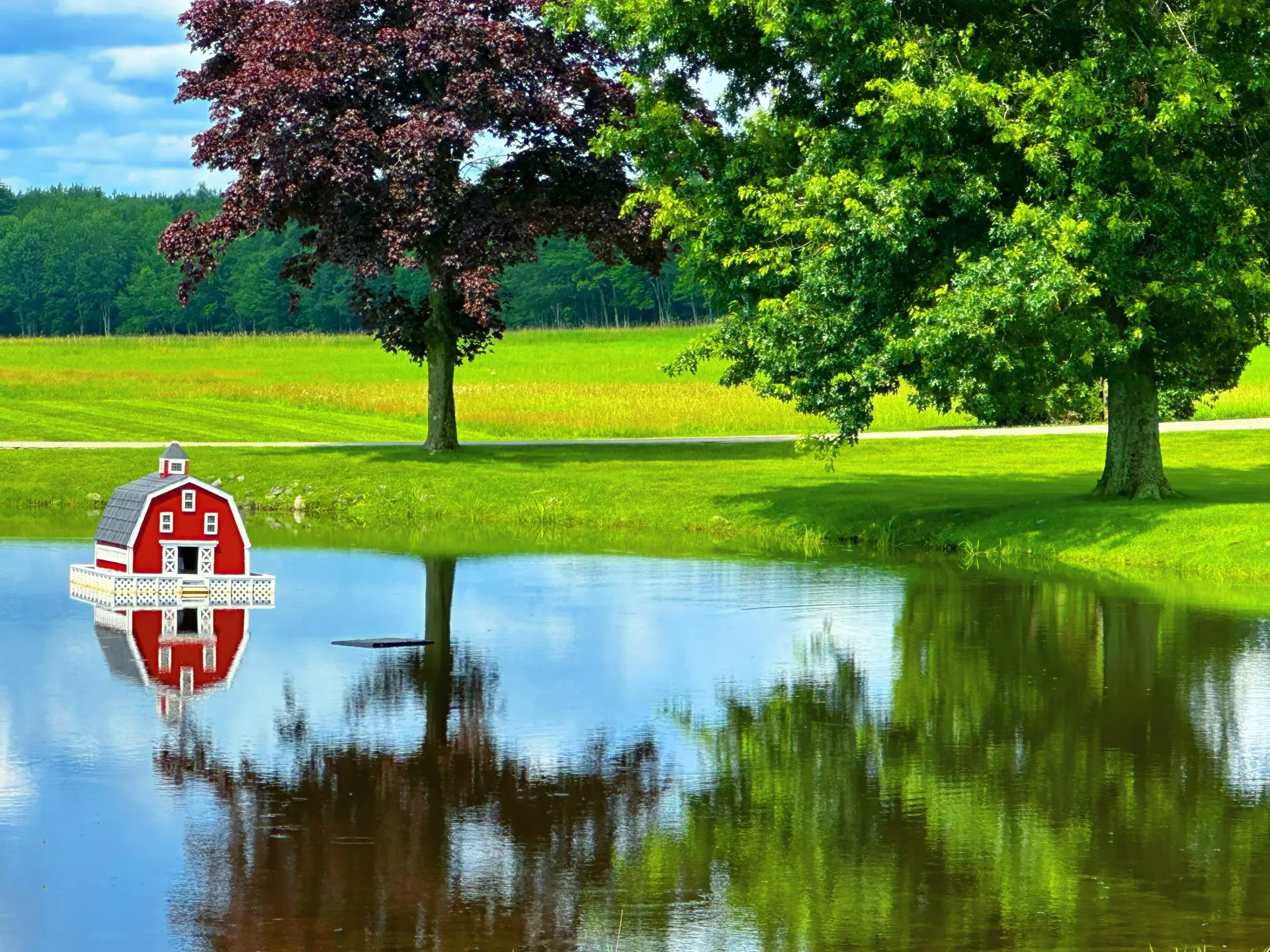A red barn is reflected in the water of a pond