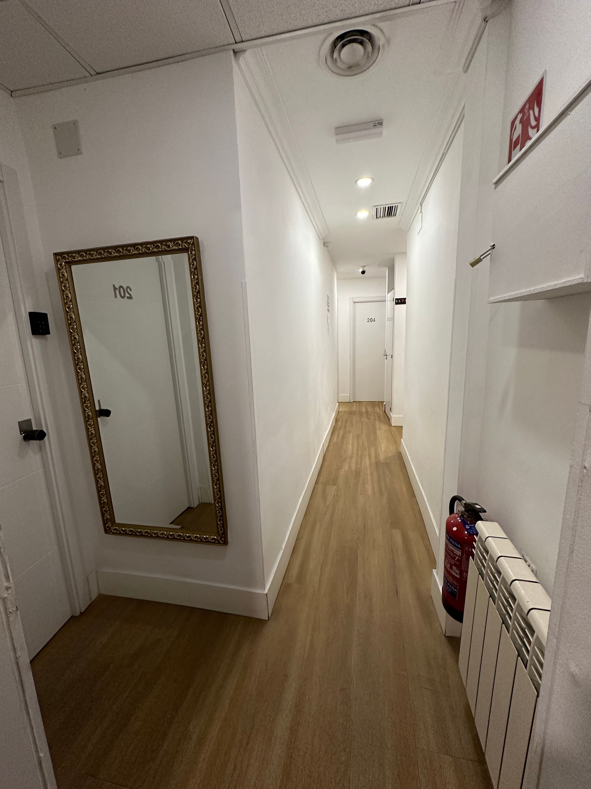 Un largo pasillo con un espejo y un extintor de incendios.