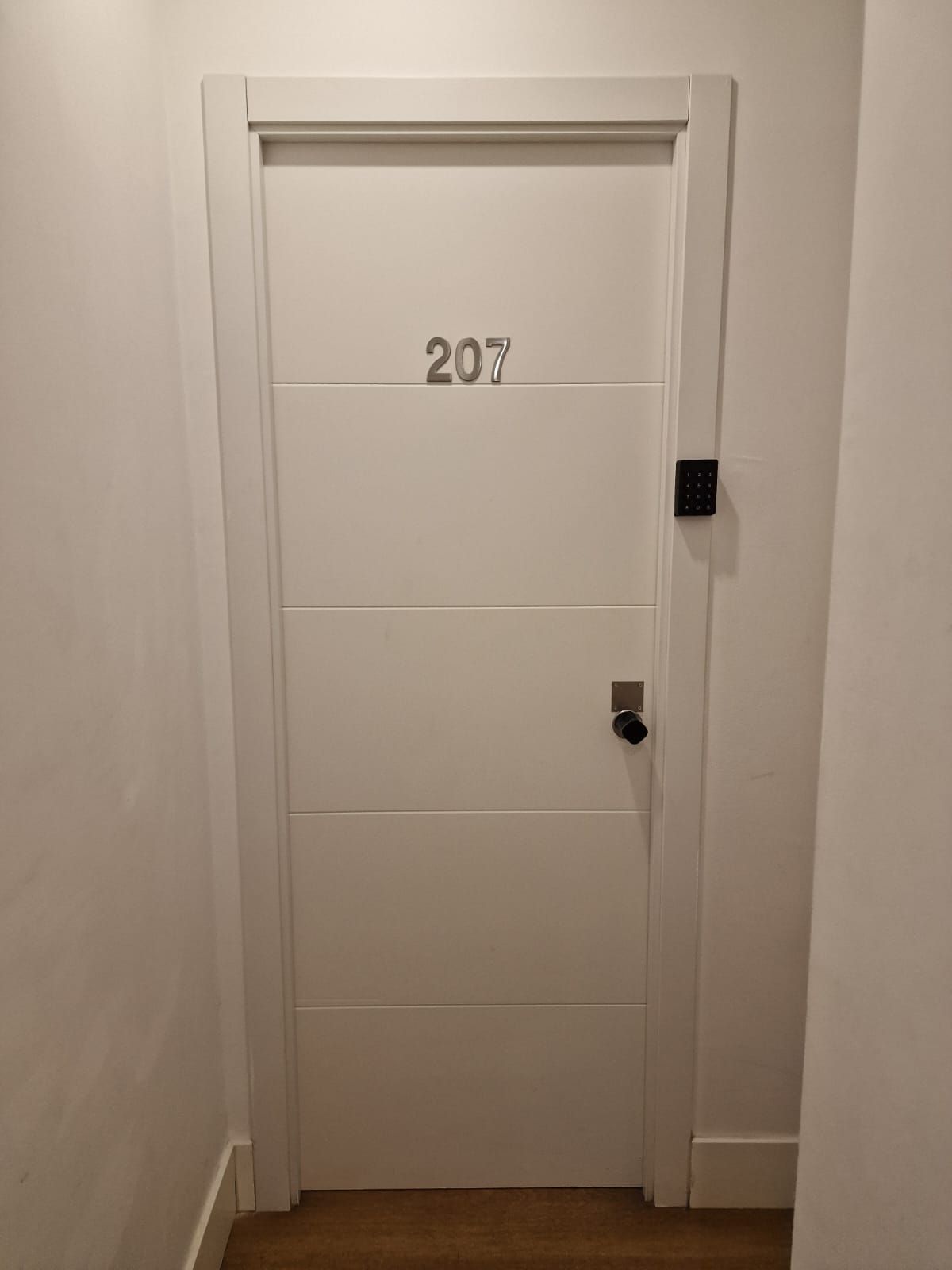 Una puerta blanca con el número 207 está en un pasillo.