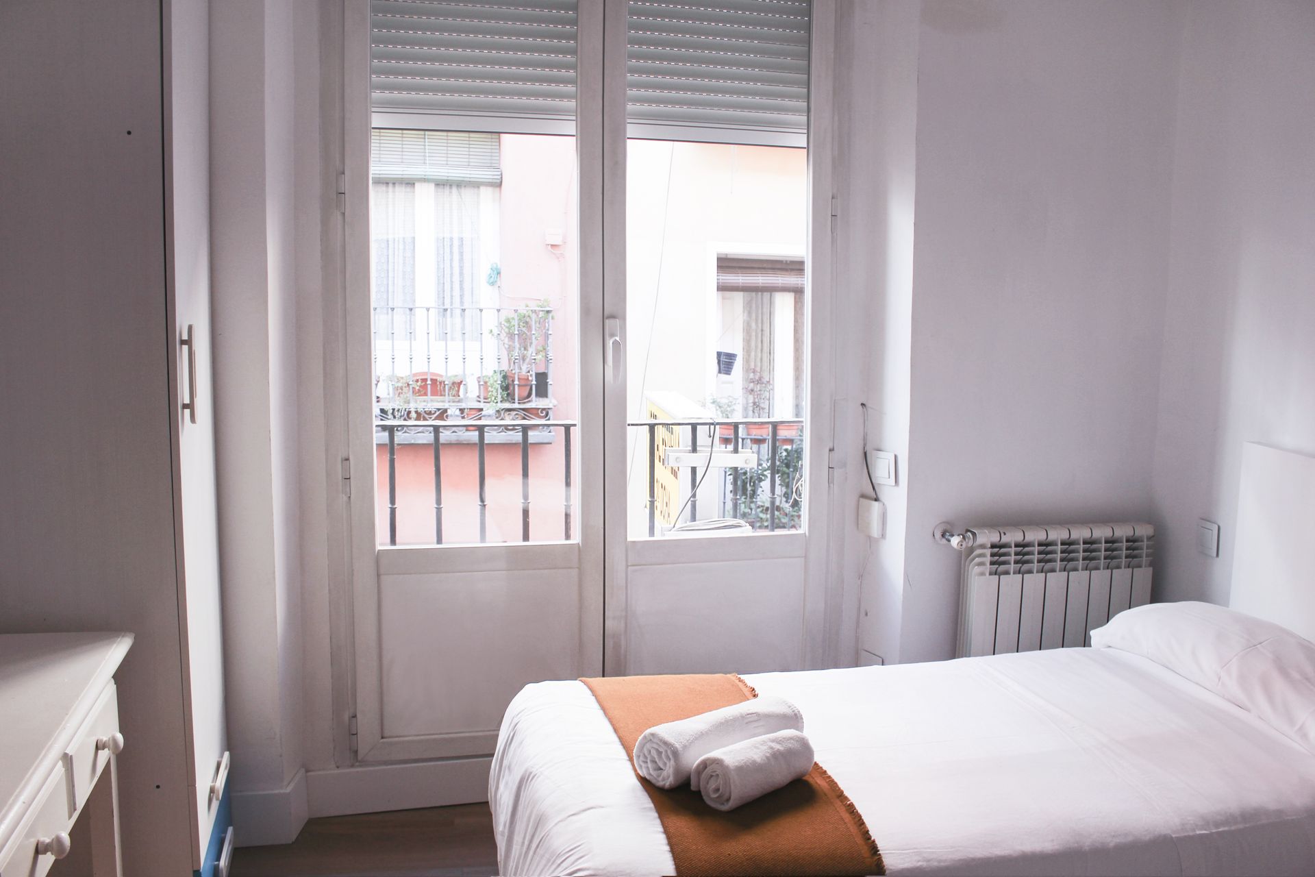 Un dormitorio con una cama, un radiador y un balcón.