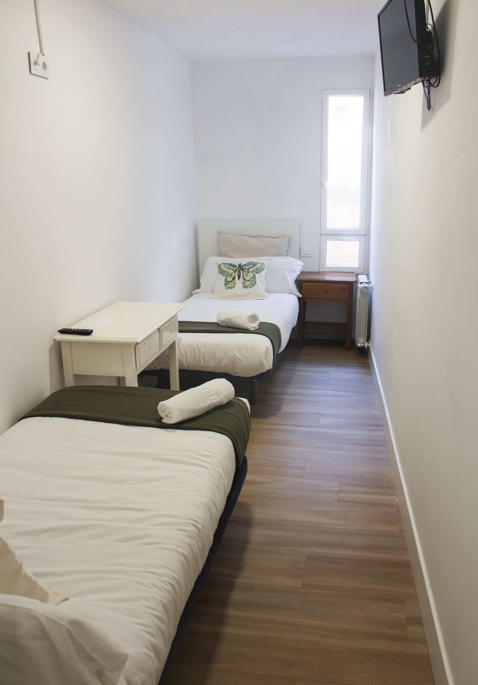 Un dormitorio pequeño con dos camas, un escritorio y una televisión.