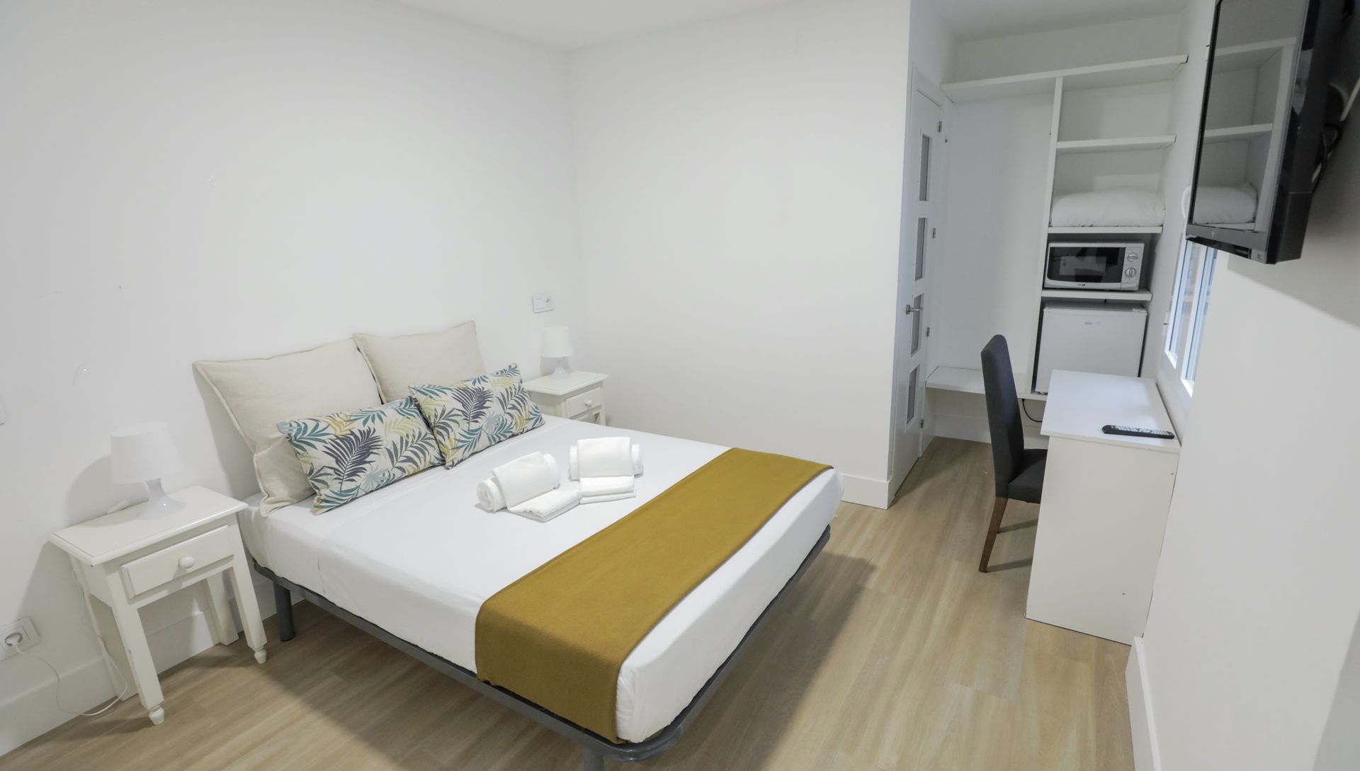 Un dormitorio con una cama, escritorio, silla y televisión.