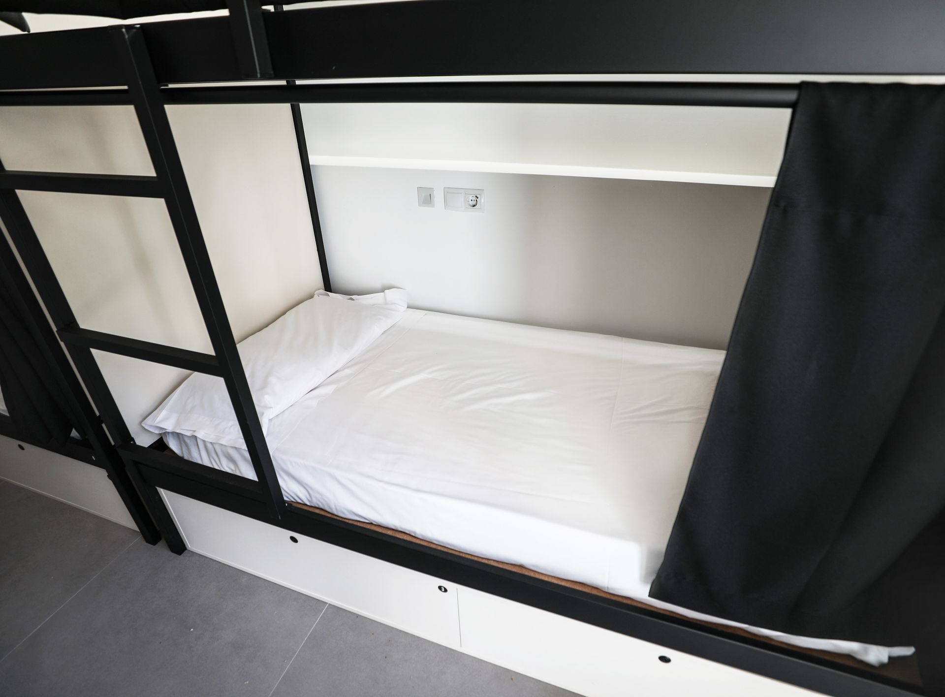 Una litera con sábanas blancas y cortinas negras