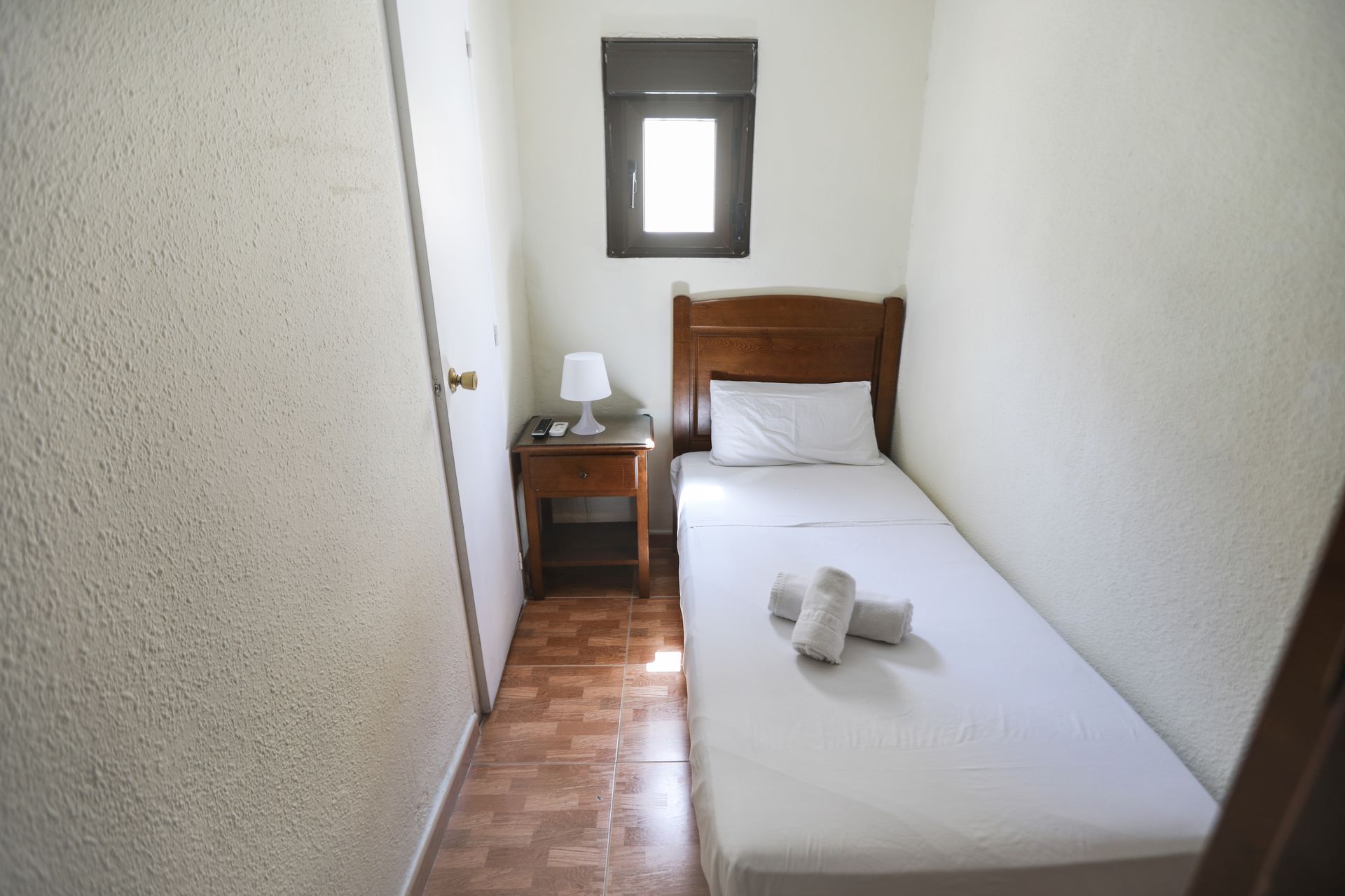 Un dormitorio pequeño con una cama individual, mesita de noche y ventana.