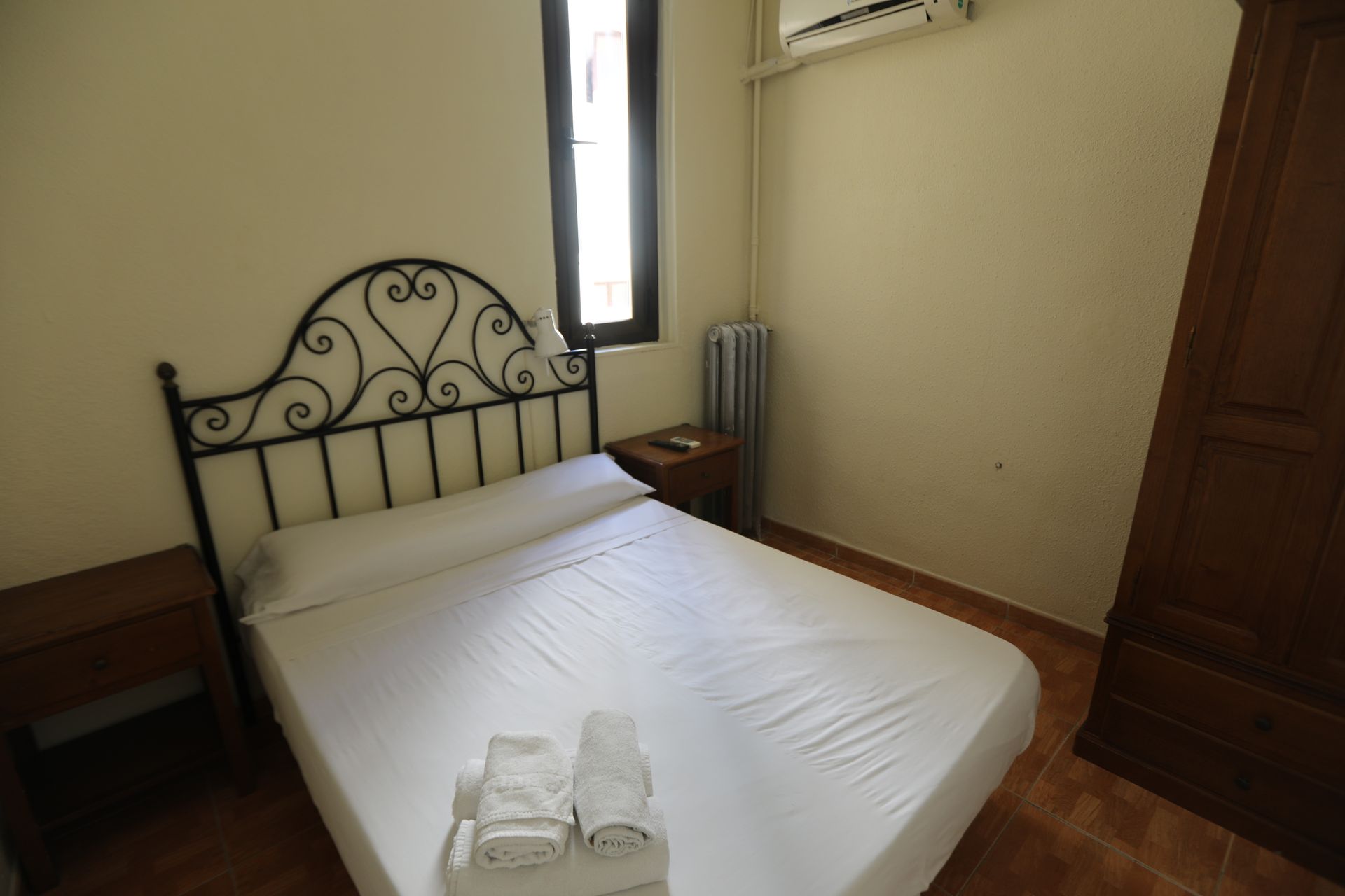 Un dormitorio con cama, mesita de noche y ventana.