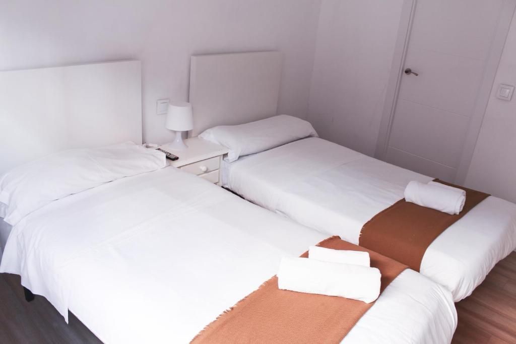 Dos camas en una habitación de hotel con sábanas blancas y mantas marrones.