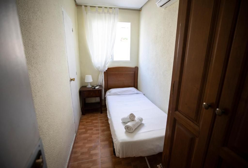 Un dormitorio pequeño con una cama individual, mesita de noche y ventana.