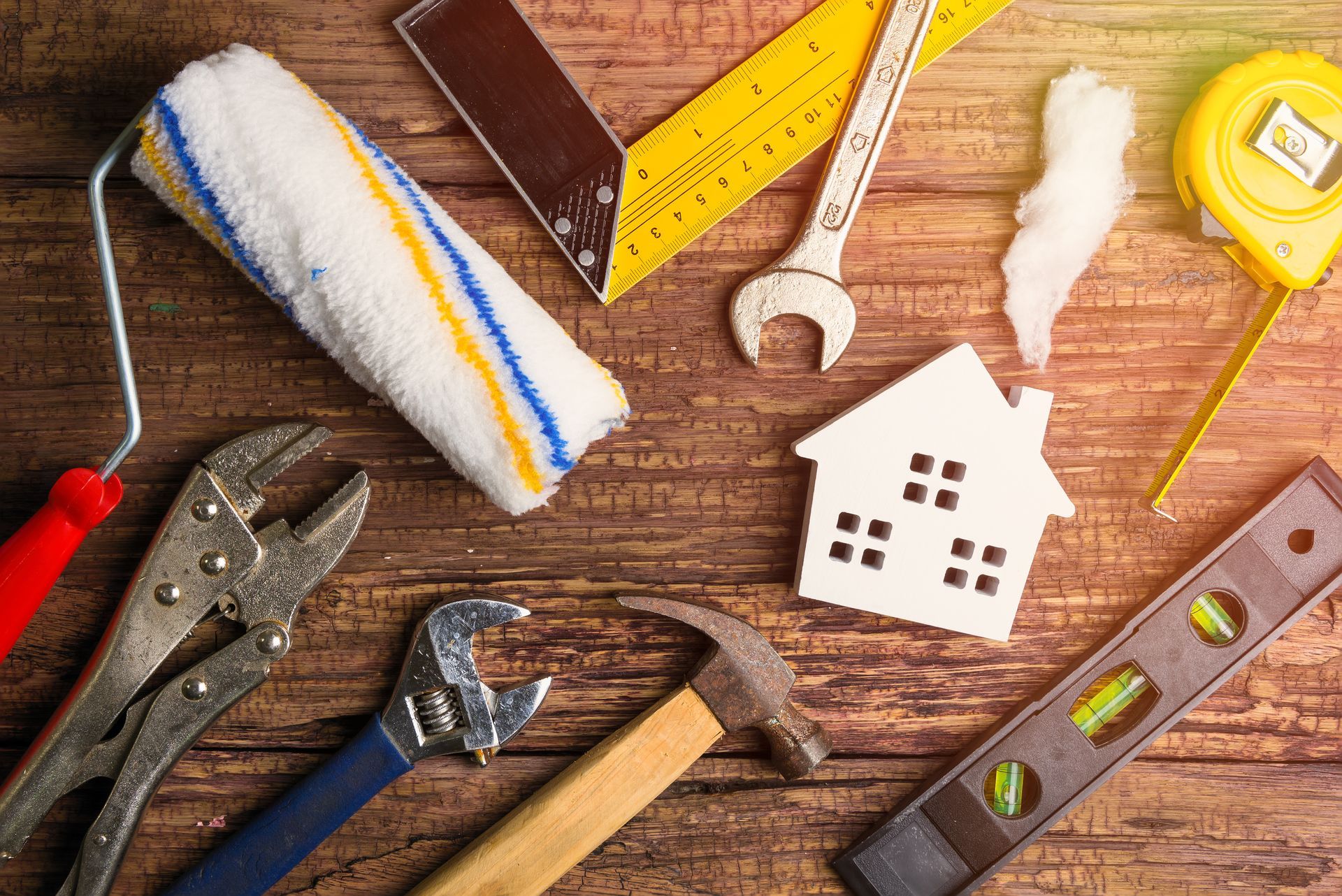 A variety of home repair tools, including a paint roller, wrench, hammer, level, and measuring tape on a wooden surface.