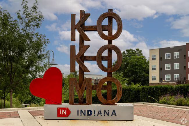 A panoramic view of a city skyline with a river in the foreground, surrounded by autumn trees under a clear blue sky.